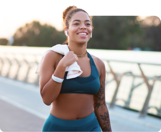 A woman in athletic wear is smiling while walking outdoors
